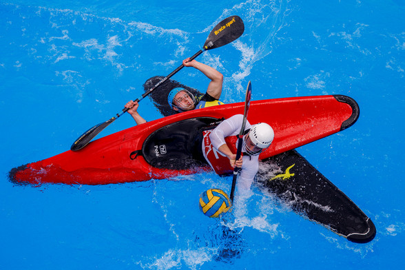 Zwei Kanupolp Spieler liegen mit ihren Booten übereinander im Wasser und kämpfen um den Ball