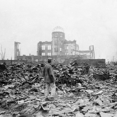 Ein Mensch steht vor dem Genbaku Dome. Es ist das einzige Gebäude, das im Areal noch steht. Überall liegen Trümmer